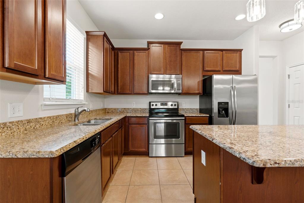 A kitchen features wood cabinets, granite countertops, stainless steel appliances, and tile flooring — 4850 SOUTHLAWN AVENUE, ORLANDO, FL
