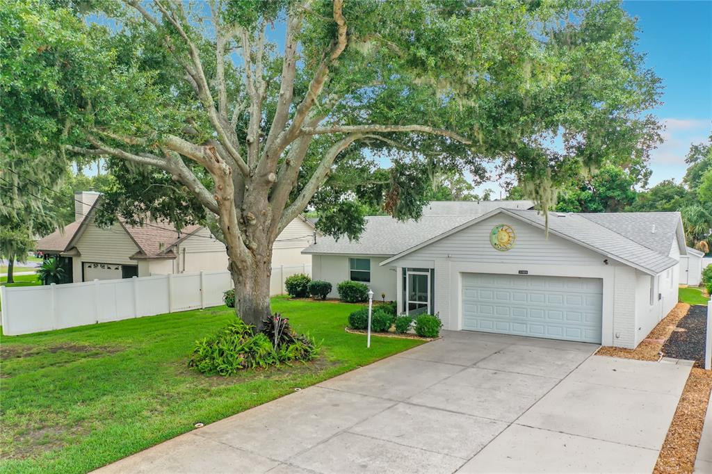 A single-story house with a white garage, gray roof, and a large tree in the yard — 33909 LINDA LANE, LEESBURG, FL