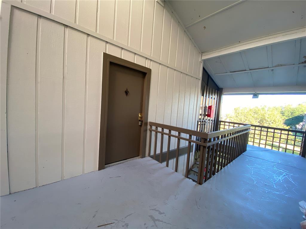 An exterior view of a brown apartment door on a covered balcony with wooden railings — 6519 W NEWBERRY ROAD UNIT 1211, GAINESVILLE, FL