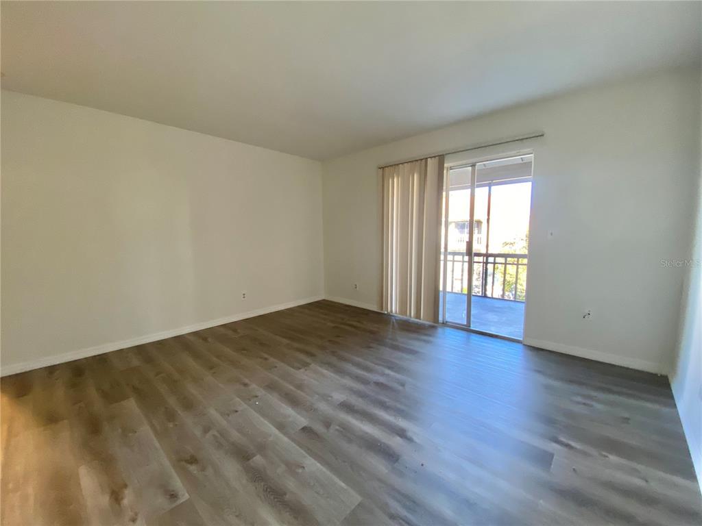 An empty living room with light-colored walls, wood-look flooring, and a sliding glass door — 6519 W NEWBERRY ROAD UNIT 1211, GAINESVILLE, FL