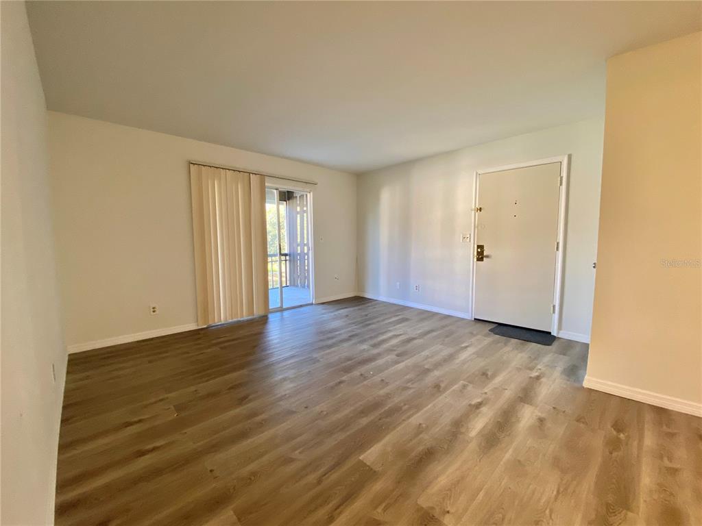 An empty living room features light-colored walls, wood-look flooring, a sliding glass door, and an entrance — 6519 W NEWBERRY ROAD UNIT 1211, GAINESVILLE, FL