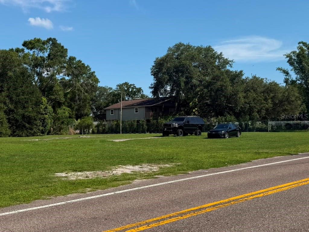 A grassy vacant lot sits next to a road with two parked vehicles and trees — 8844 S MOBLEY ROAD, TAMPA, FL