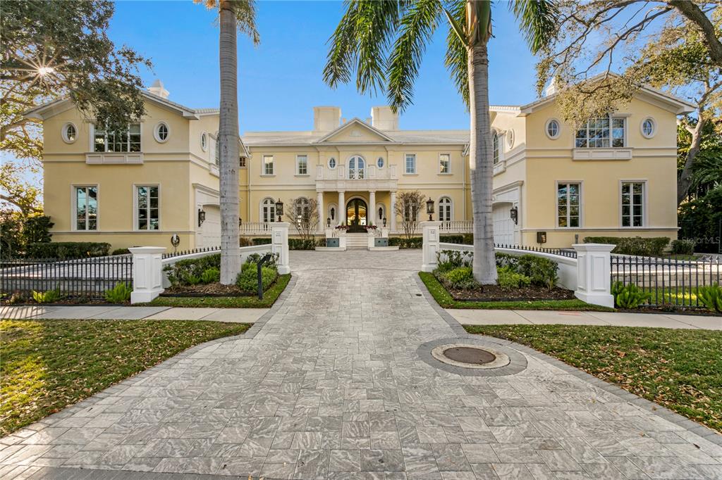 A large, yellow, two-story mansion features a stone driveway, palm trees, and a gated entrance — 52 LADOGA AVENUE, TAMPA, FL