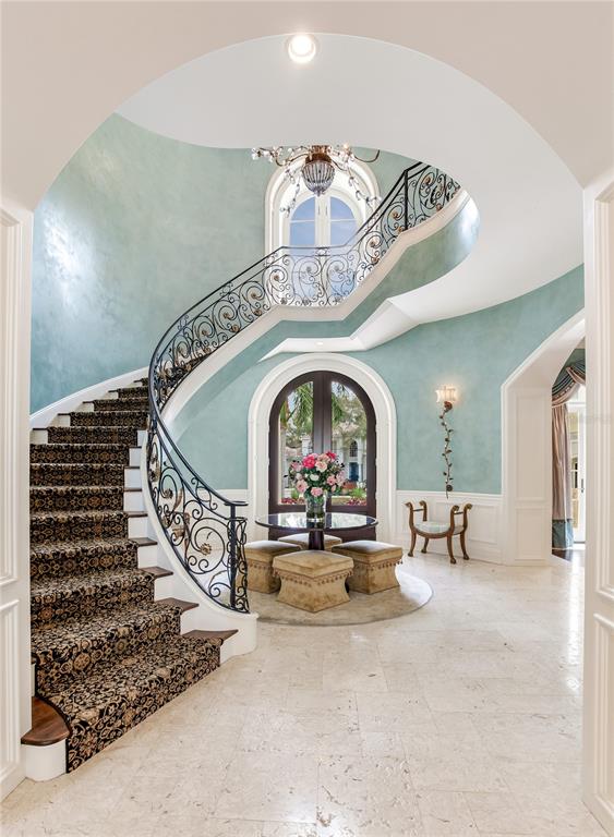 A grand foyer features a curved staircase with ornate iron railings and light blue walls — 52 LADOGA AVENUE, TAMPA, FL