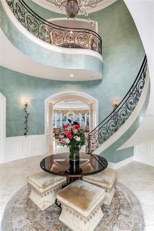 A grand foyer features a curved staircase, a central table with ottomans, and blue walls — 52 LADOGA AVENUE, TAMPA, FL