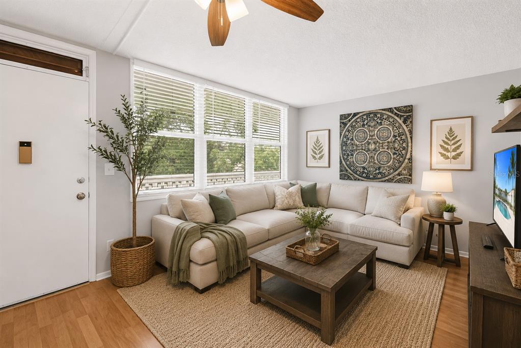 A living room features a beige sectional sofa, a wooden coffee table, and a large window — 4720 LOCUST STREET NE UNIT 318, ST PETERSBURG, FL