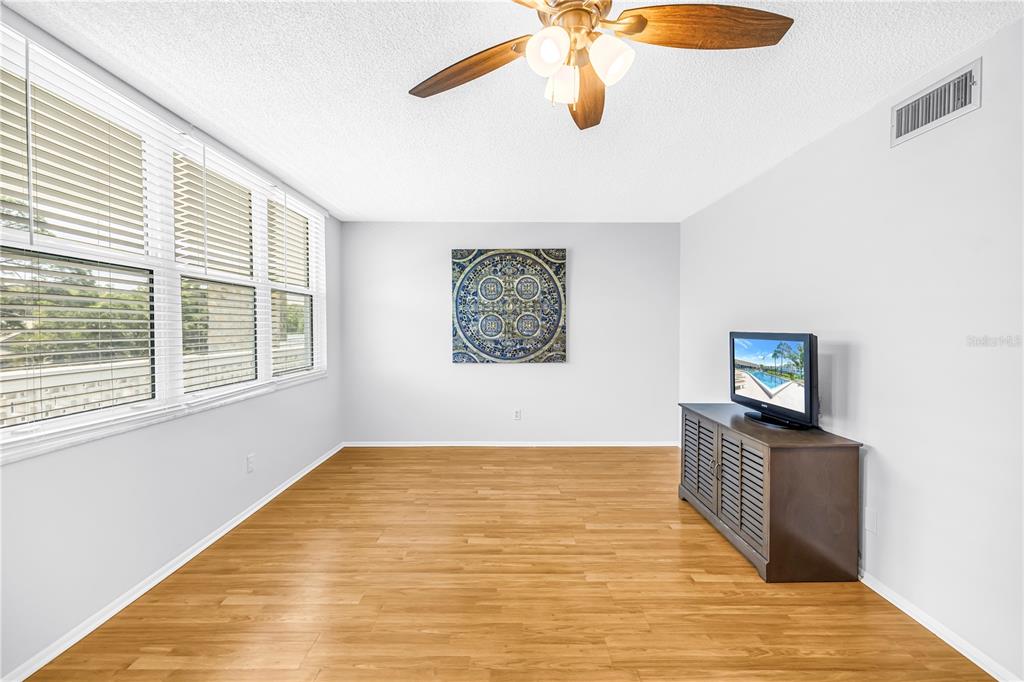 A bright room features light wood flooring, a ceiling fan, and a television on a console — 4720 LOCUST STREET NE UNIT 318, ST PETERSBURG, FL