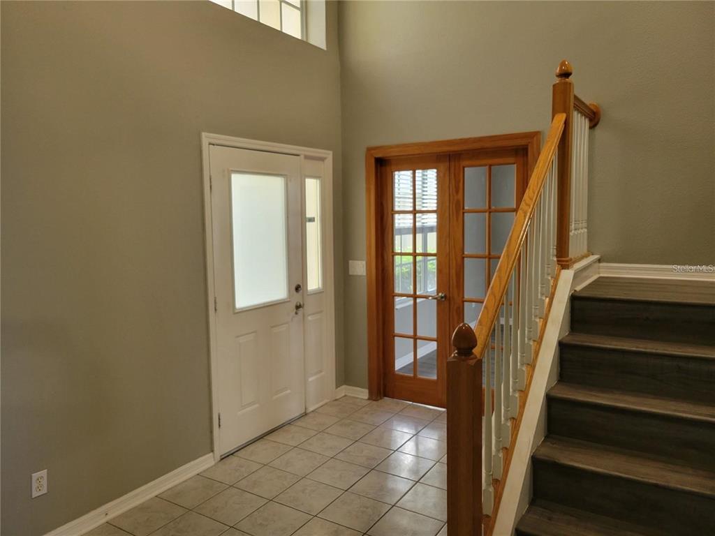 An entryway features a white front door, French doors, and a staircase with wooden railings — 7215 COLONIAL LAKE DRIVE, RIVERVIEW, FL
