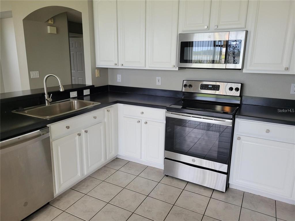 A kitchen features white cabinets, black countertops, stainless steel appliances, and light-colored tile flooring — 7215 COLONIAL LAKE DRIVE, RIVERVIEW, FL
