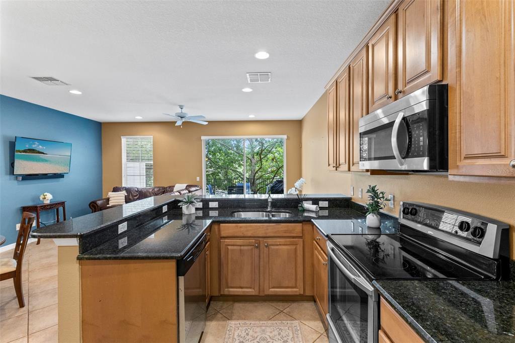A kitchen with wood cabinets and black countertops overlooks an adjacent living area — 5128 CYPRESS BRANCH POINT, OVIEDO, FL