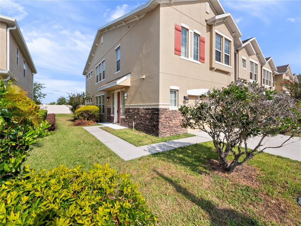 A tan two-story townhouse with stone veneer siding and red shutters on a sunny day — 1610 MOHEGAN BOULEVARD, KISSIMMEE, FL