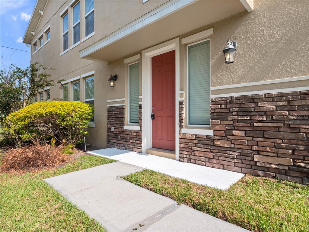 The exterior of a house features a red front door, stone siding, and a walkway — 1610 MOHEGAN BOULEVARD, KISSIMMEE, FL