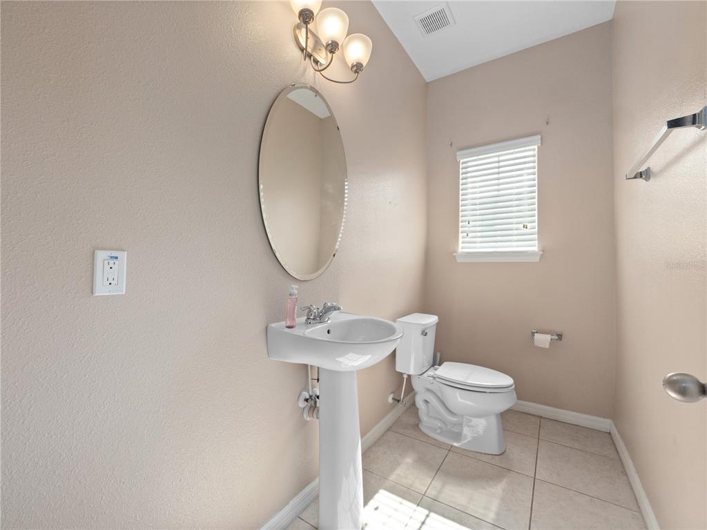 A bathroom features a pedestal sink, an oval mirror, a toilet, and beige walls — 1610 MOHEGAN BOULEVARD, KISSIMMEE, FL