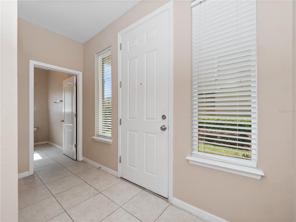 An entryway features beige tile flooring, a white front door, and two windows with blinds — 1610 MOHEGAN BOULEVARD, KISSIMMEE, FL