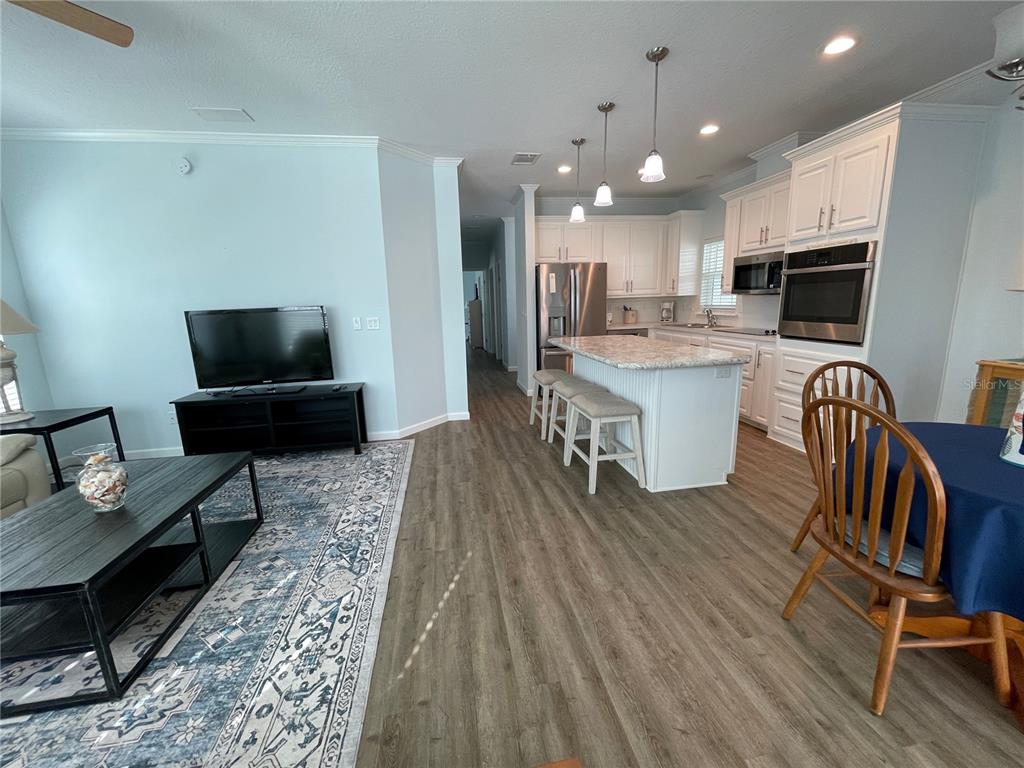 An open-concept living room and kitchen feature light wood flooring, white cabinetry, and an island — 612 CAREFREE, VENICE, FL
