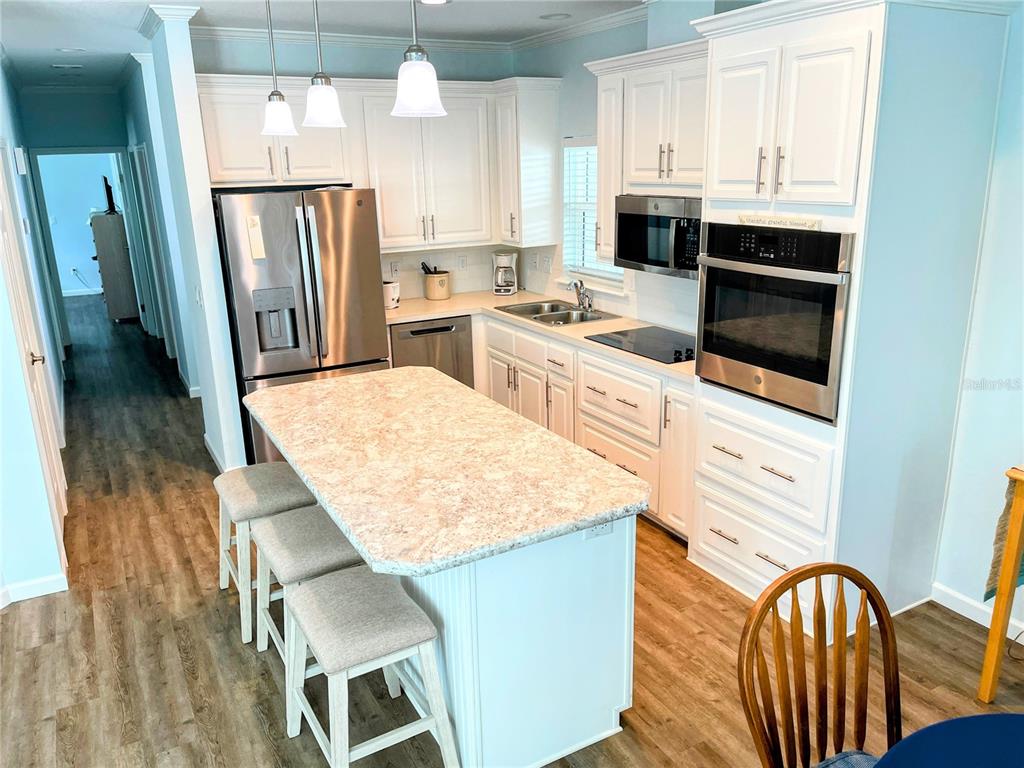 A kitchen features white cabinets, stainless steel appliances, a stone island, and light wood flooring — 612 CAREFREE, VENICE, FL