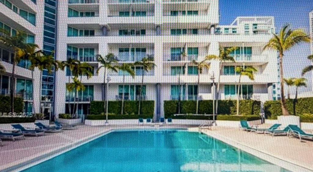 A rectangular swimming pool sits in front of a multi-story white apartment building with balconies — 350 NE 24TH STREET UNIT 514, MIAMI, FL