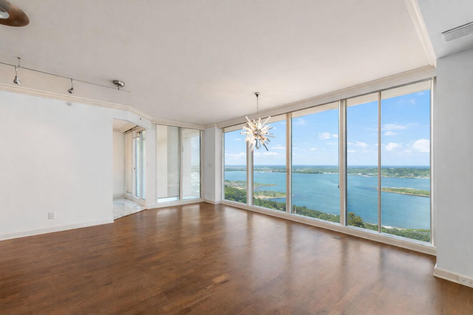 An empty living room with hardwood floors, a modern chandelier, and floor-to-ceiling windows overlooking water — 529 S Flagler Drive, West Palm Beach FL 33401, WEST PALM BEACH, FL