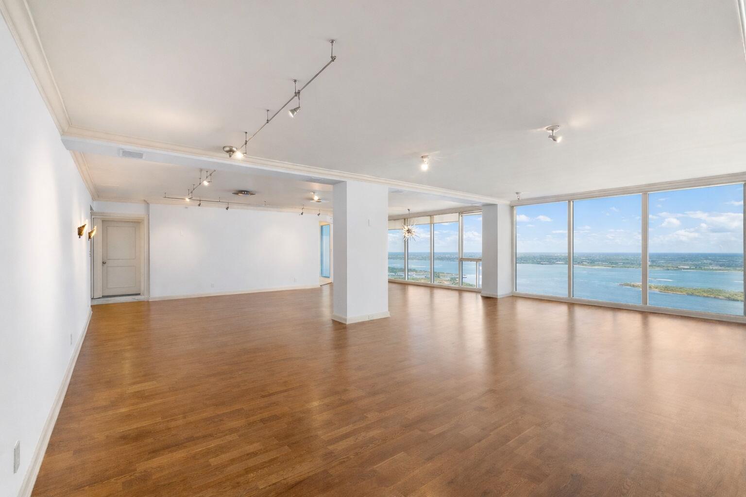 An empty room with hardwood floors, white walls, track lighting, and floor-to-ceiling windows overlooking water — 529 S Flagler Drive, West Palm Beach FL 33401, WEST PALM BEACH, FL