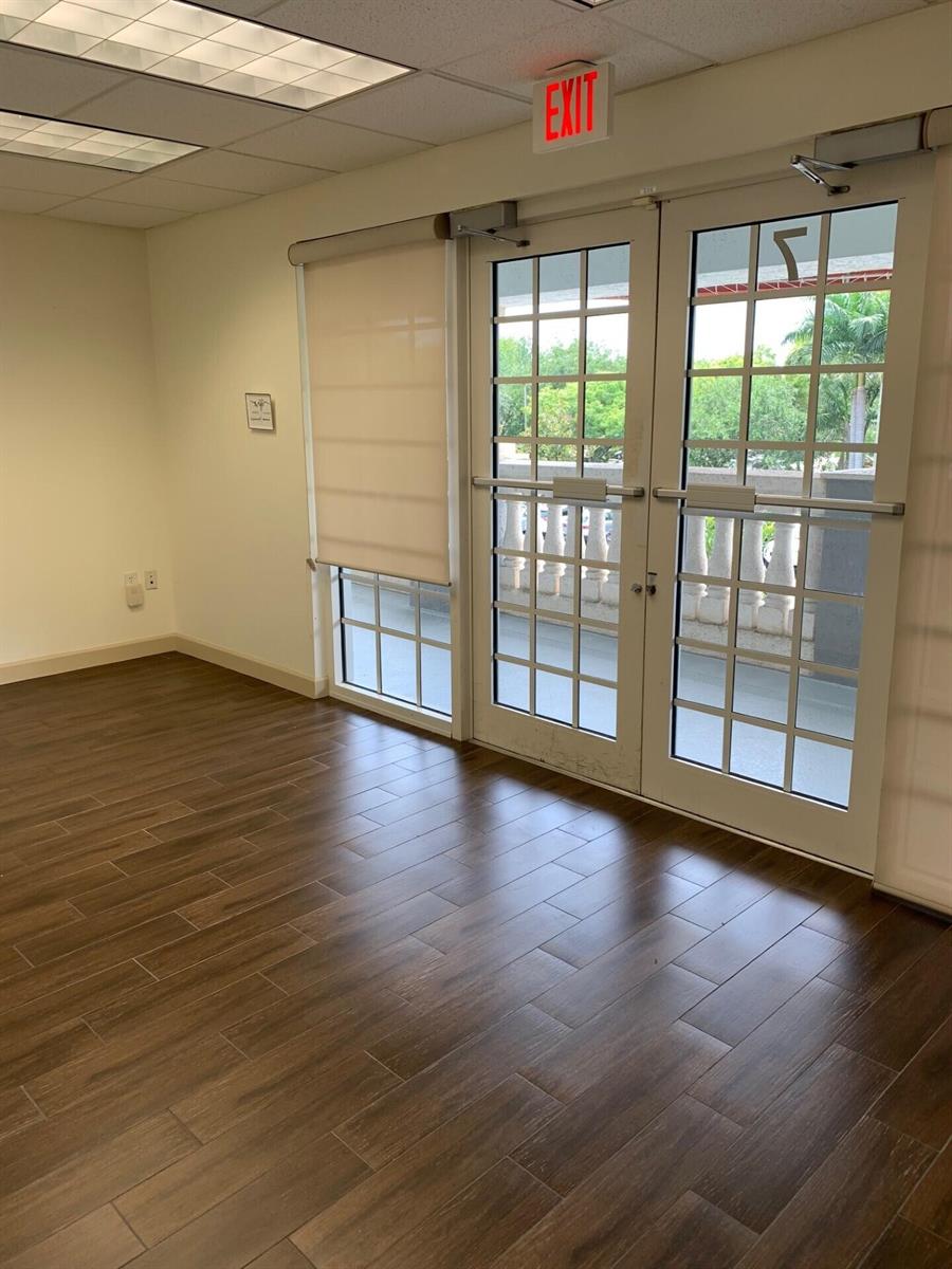 An empty room with wood-look tile flooring, a roller shade, and double glass exit doors — 2225 N Commerce Parkway # 7, Weston FL 33326, WESTON, FL