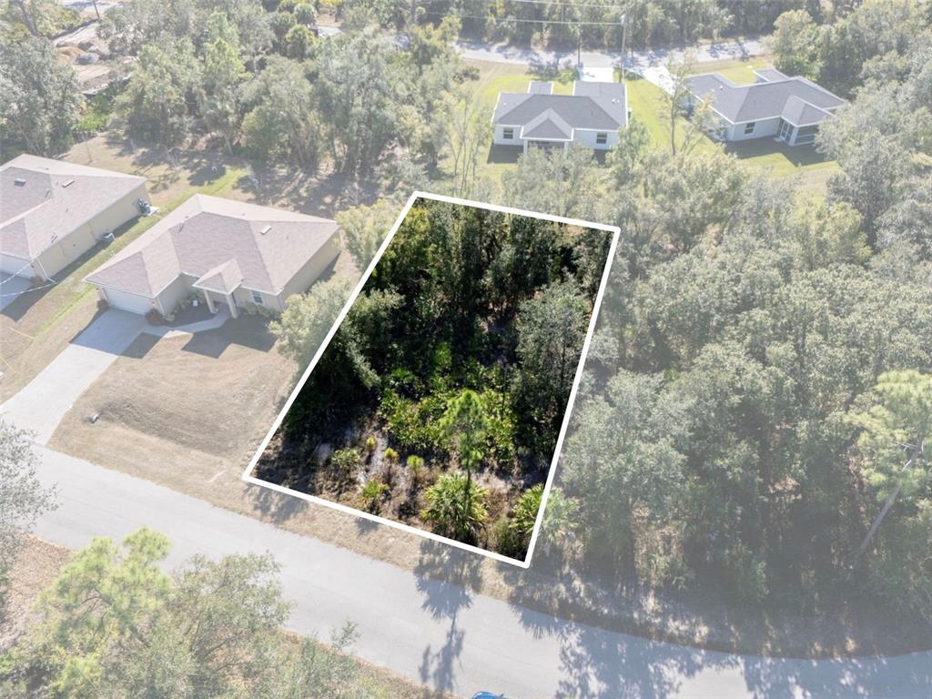 An aerial view shows a wooded, rectangular vacant lot situated between two residential houses — JODY AVENUE, NORTH PORT, FL