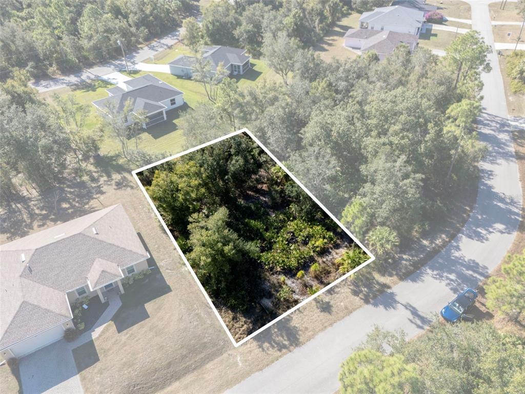 An aerial view shows a wooded, rectangular vacant lot situated between two residential houses — JODY AVENUE, NORTH PORT, FL