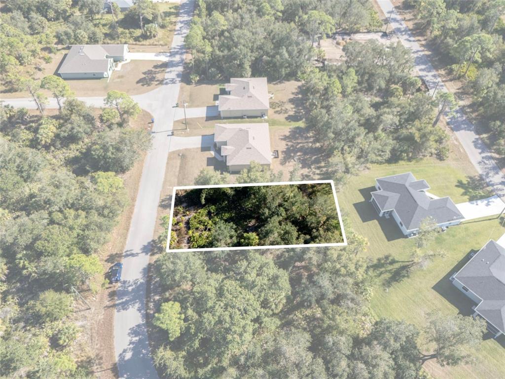 An aerial view shows a rectangular, wooded vacant lot outlined in white between residential houses — JODY AVENUE, NORTH PORT, FL