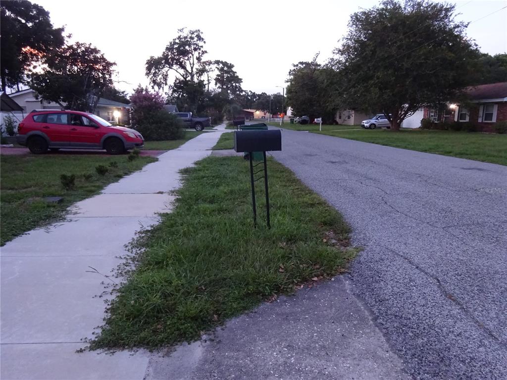 A residential street view featuring a sidewalk, a mailbox, and a parked red car — 6141 10TH STREET, ZEPHYRHILLS, FL