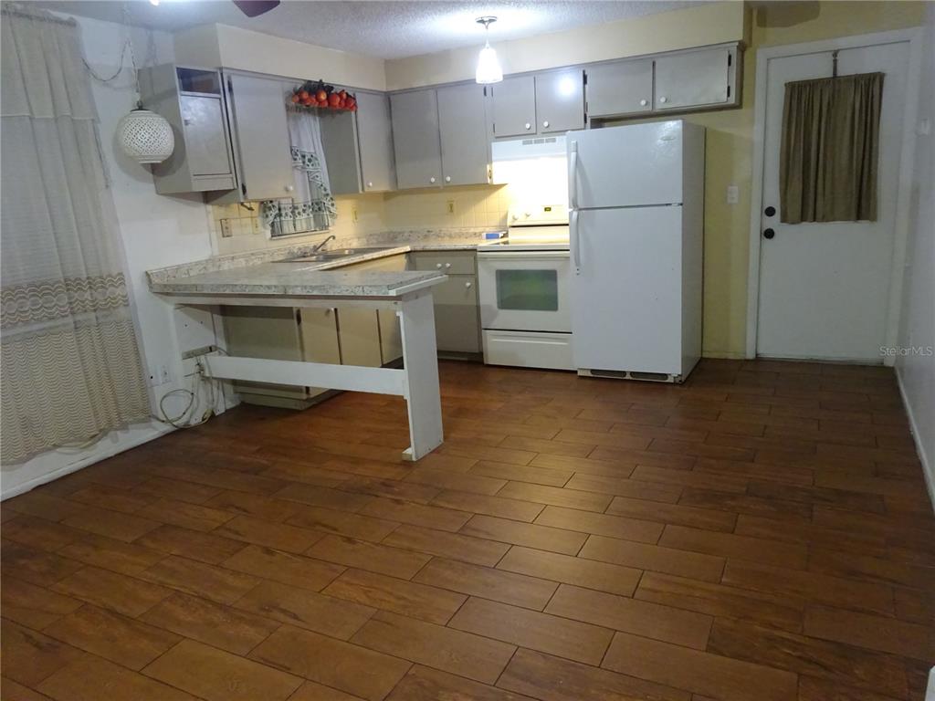 A kitchen features gray cabinets, a white stove, a white refrigerator, and wood-look tile flooring — 6141 10TH STREET, ZEPHYRHILLS, FL