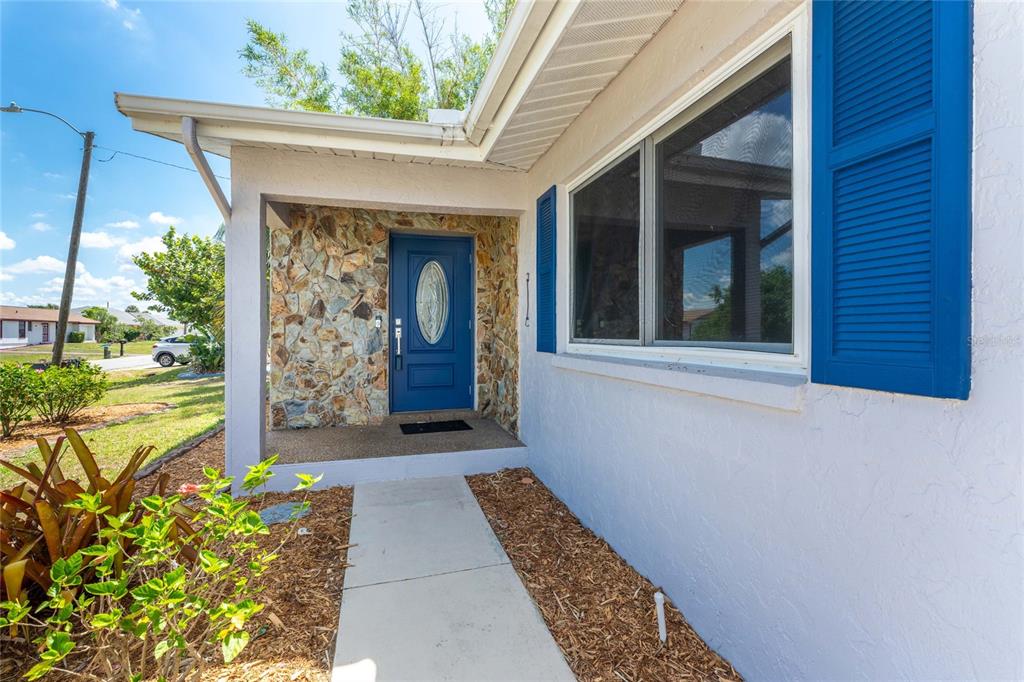 A concrete walkway leads to a blue front door set in a stone-accented entryway — 557 MAGNOLIA AVENUE NW, PORT CHARLOTTE, FL