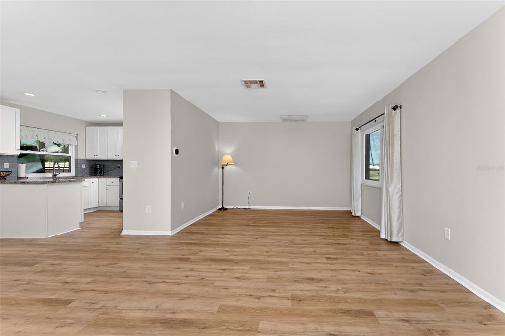 An open-concept living area features light wood-look flooring and a view into the kitchen — 557 MAGNOLIA AVENUE NW, PORT CHARLOTTE, FL