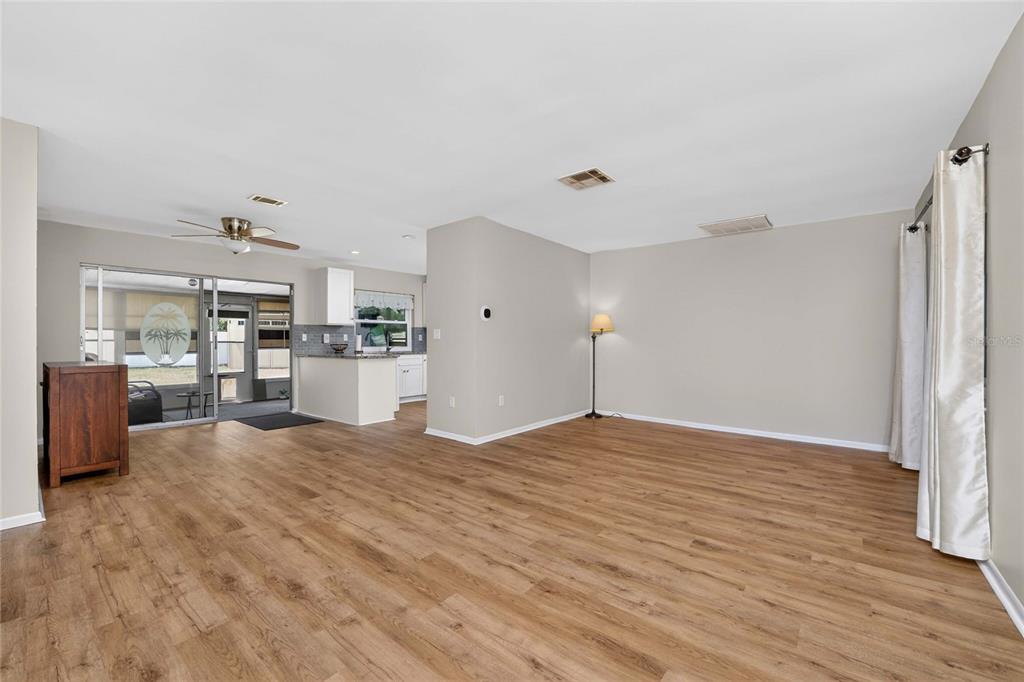 An open-concept living area features light wood-look flooring, neutral walls, and a kitchen beyond — 557 MAGNOLIA AVENUE NW, PORT CHARLOTTE, FL