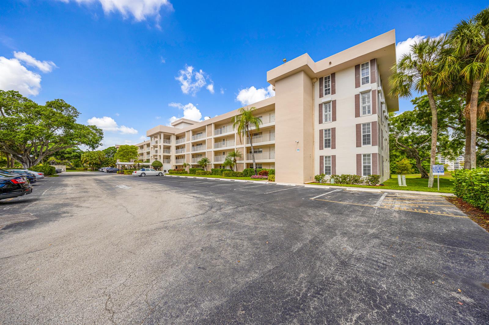 A multi-story apartment building with a parking lot in the foreground under a blue sky — 3151 S Palm Aire Drive # 407, Pompano Beach FL 33069, POMPANO BEACH, FL