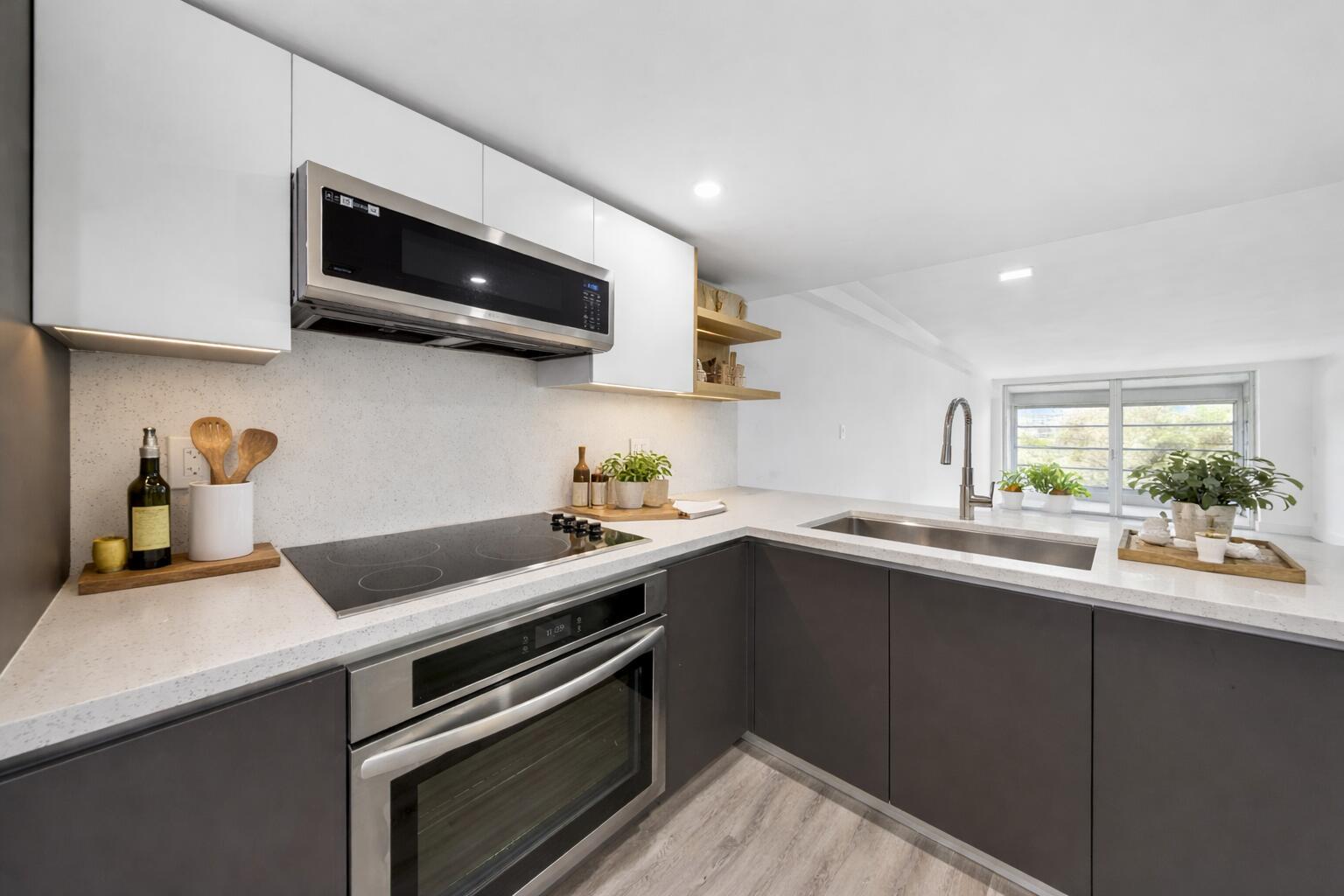 A modern kitchen features dark gray lower cabinets, white upper cabinets, and light stone countertops — 3151 S Palm Aire Drive # 407, Pompano Beach FL 33069, POMPANO BEACH, FL