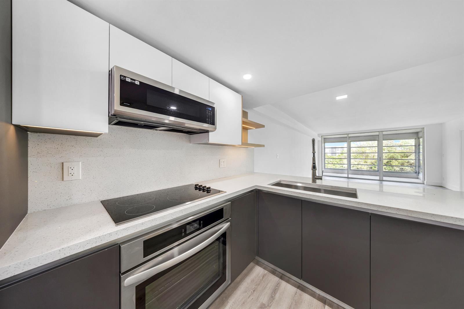 A modern kitchen features dark lower cabinets, white upper cabinets, and light quartz countertops — 3151 S Palm Aire Drive # 407, Pompano Beach FL 33069, POMPANO BEACH, FL