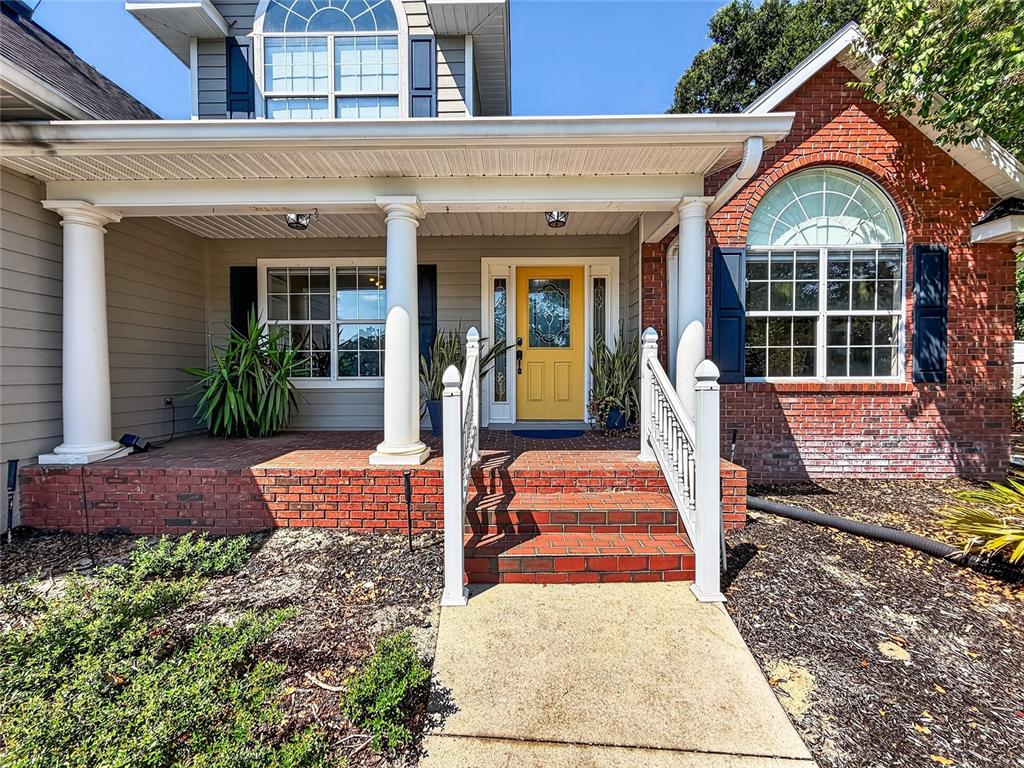 A brick-front house features a covered porch, white columns, and a bright yellow front door — 33721 SPRING DRIVE, LEESBURG, FL