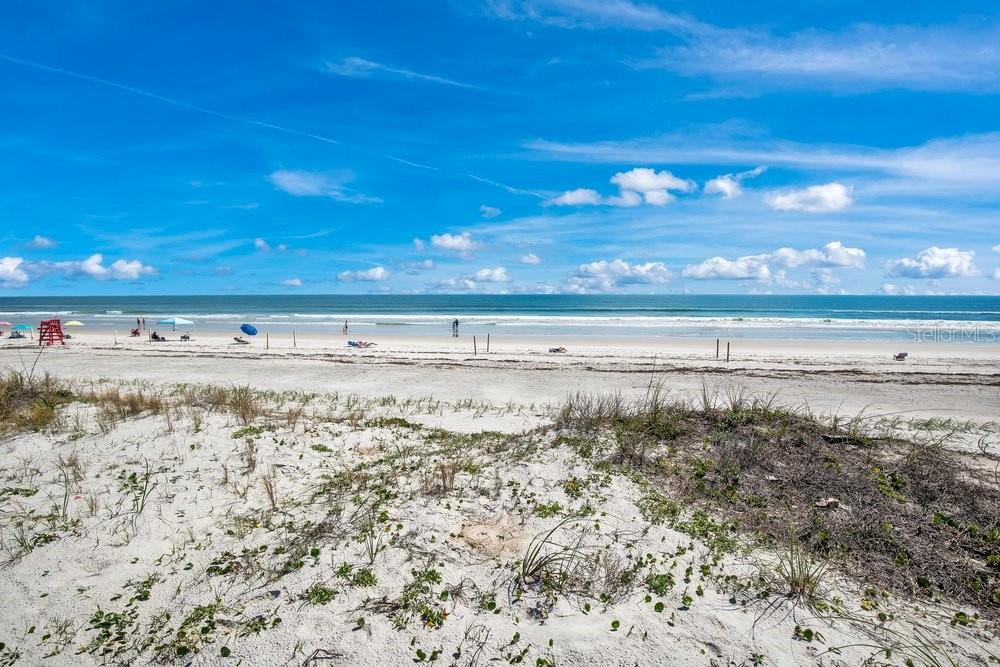A sandy beach with dunes in the foreground and the ocean under a blue sky — 4591 S ATLANTIC AVENUE, PORT ORANGE, FL