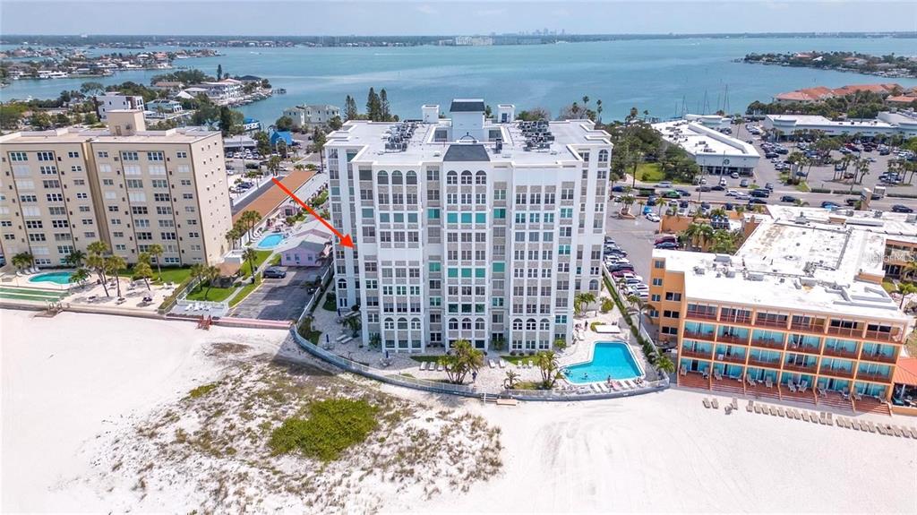 An aerial view shows a multi-story white condominium building situated on a sandy beach — 4950 GULF BOULEVARD UNIT 408, ST PETE BEACH, FL