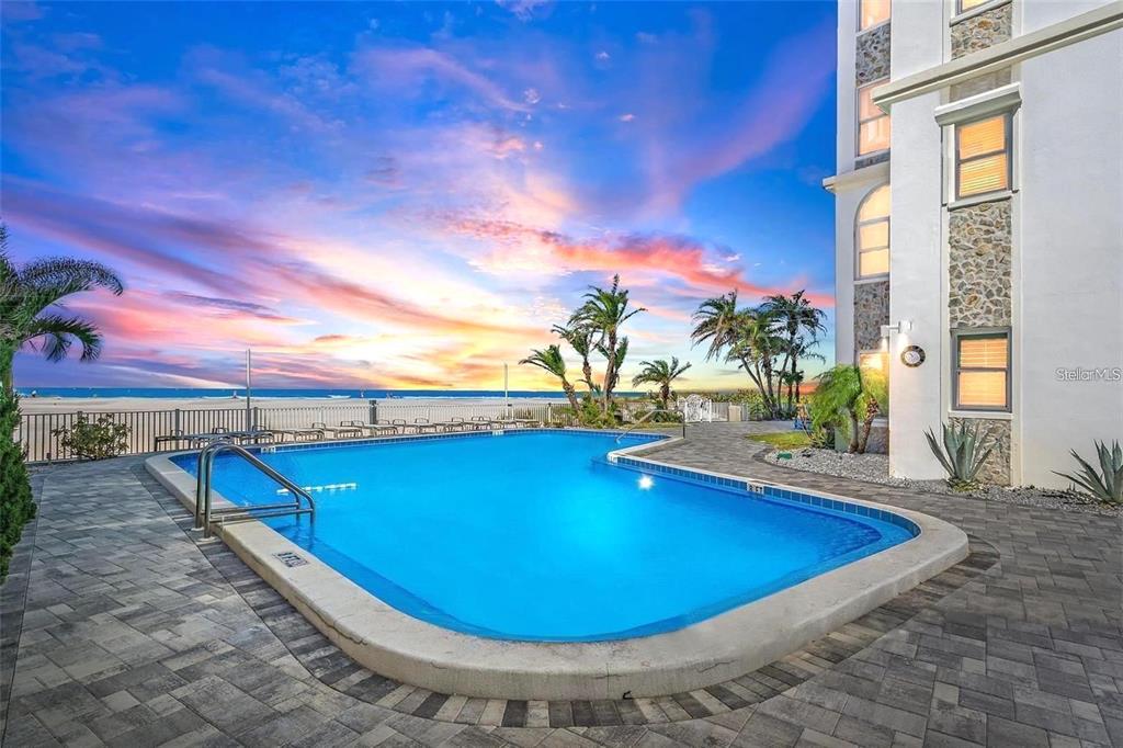 A swimming pool sits on a stone patio next to a building overlooking the beach — 4950 GULF BOULEVARD UNIT 408, ST PETE BEACH, FL