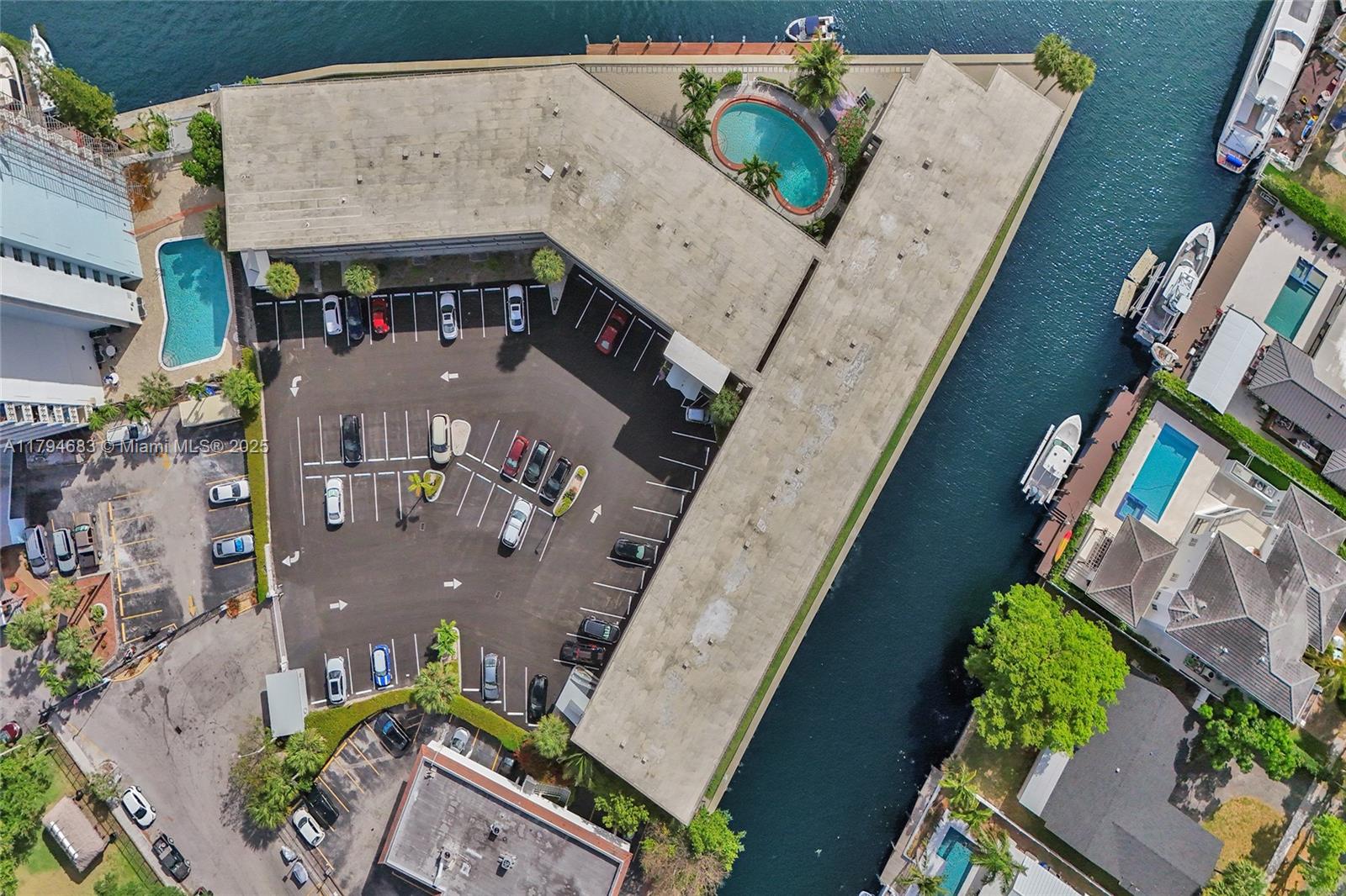 An aerial view shows a multi-story building with a parking lot, swimming pool, and canal — 13105 Ixora Ct # 319, North Miami FL 33181, NORTH MIAMI, FL