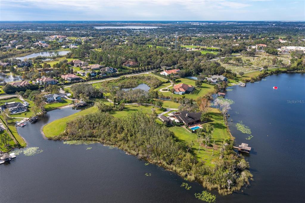 An aerial view shows a waterfront house with a pool on a grassy peninsula — 13377 LAKE BUTLER BOULEVARD, WINTER GARDEN, FL