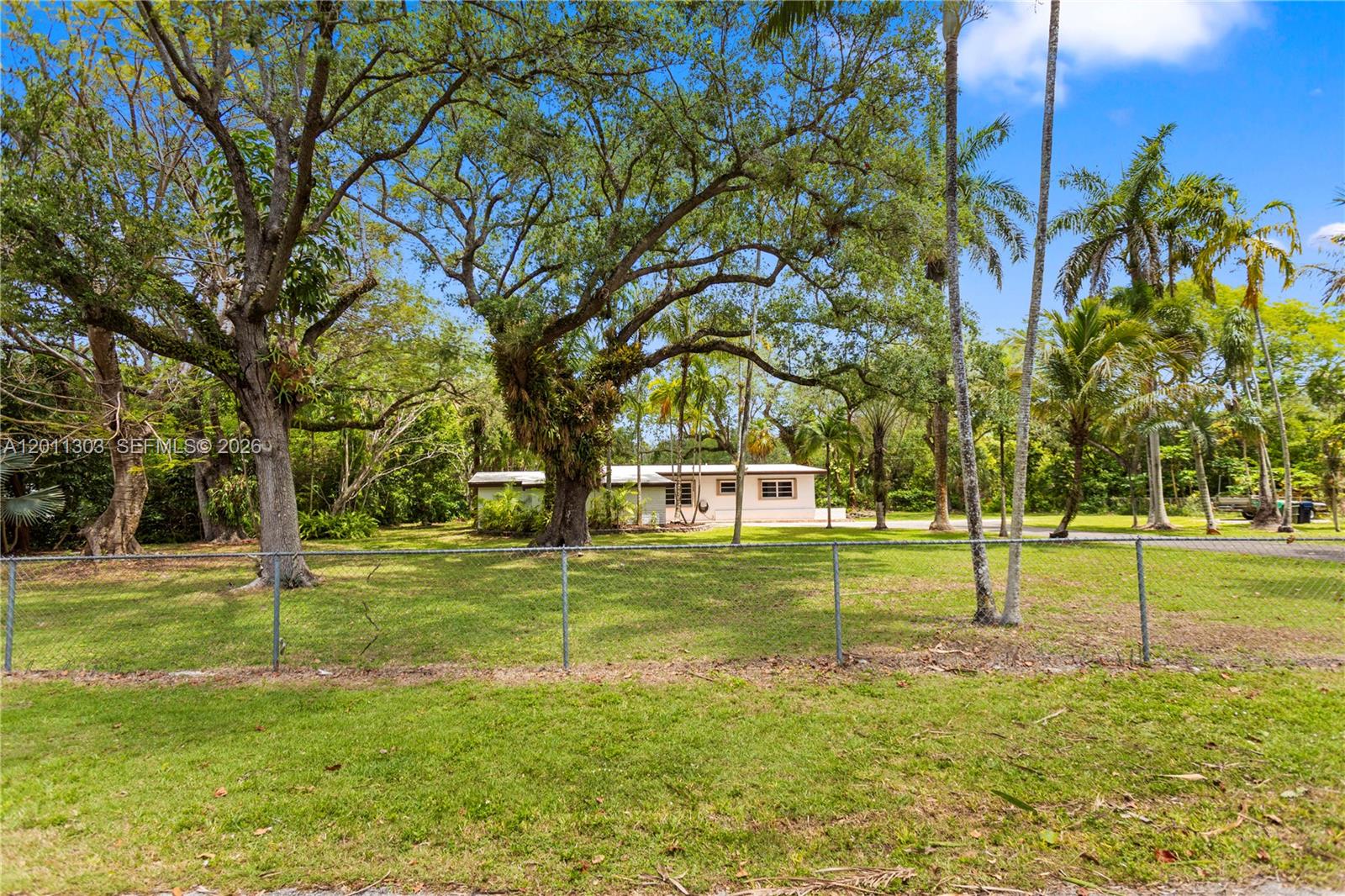 A single-story house sits behind a chain-link fence on a large, tree-filled grassy lot — 15345 SW 269th Ter, Homestead FL 33032, HOMESTEAD, FL