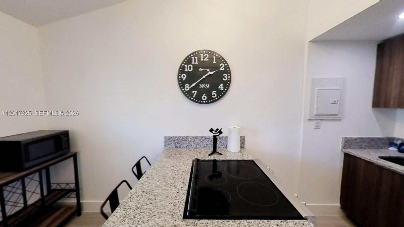 A kitchen features a granite countertop island with a built-in cooktop and a wall clock — 840 SW 7th St # 852, Miami FL 33130, MIAMI, FL