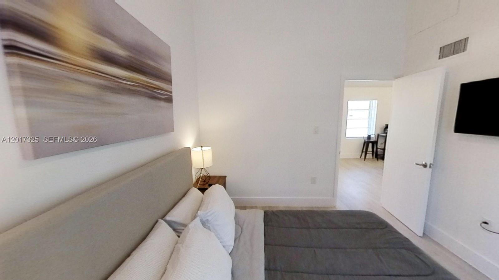 A bedroom features a bed with a gray comforter, a wall-mounted television, and an open doorway — 840 SW 7th St # 852, Miami FL 33130, MIAMI, FL