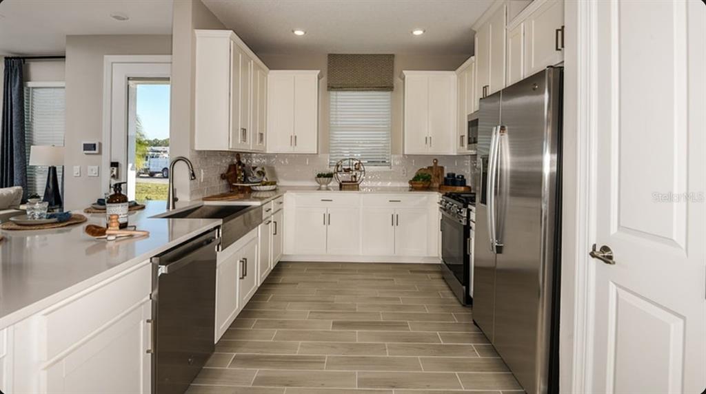A kitchen features white cabinets, stainless steel appliances, a farmhouse sink, and wood-look tile flooring — 5380 SPOONFLOWER COURT, ST CLOUD, FL