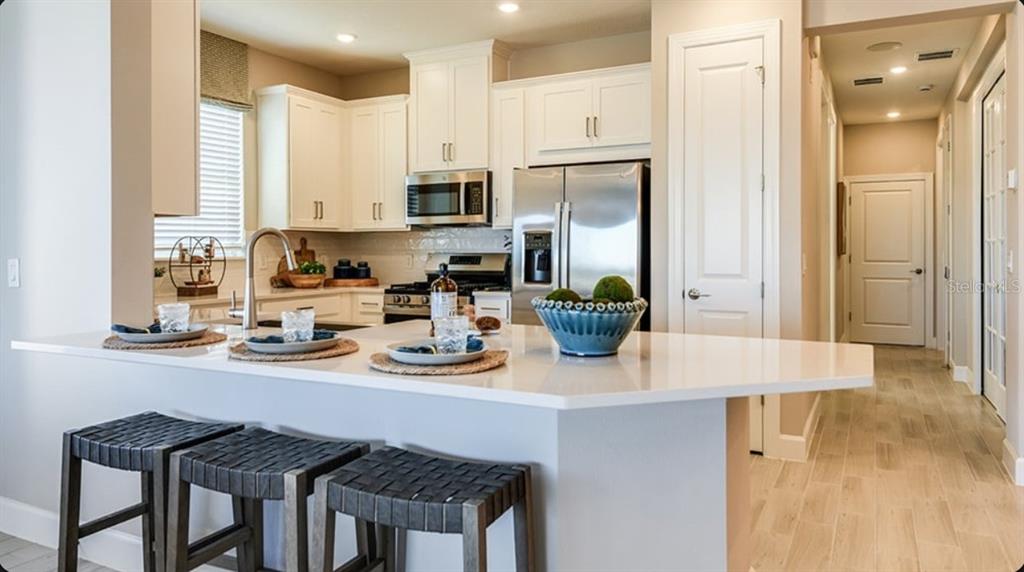 A kitchen features white cabinets, stainless steel appliances, a quartz island, and three bar stools — 5380 SPOONFLOWER COURT, ST CLOUD, FL