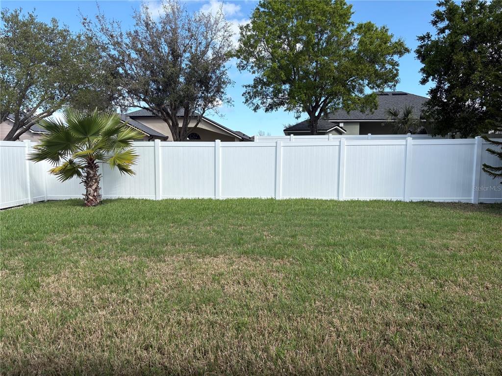 A grassy backyard features a white vinyl privacy fence and a small palm tree — 1150 CREEKVIEW, ST CLOUD, FL