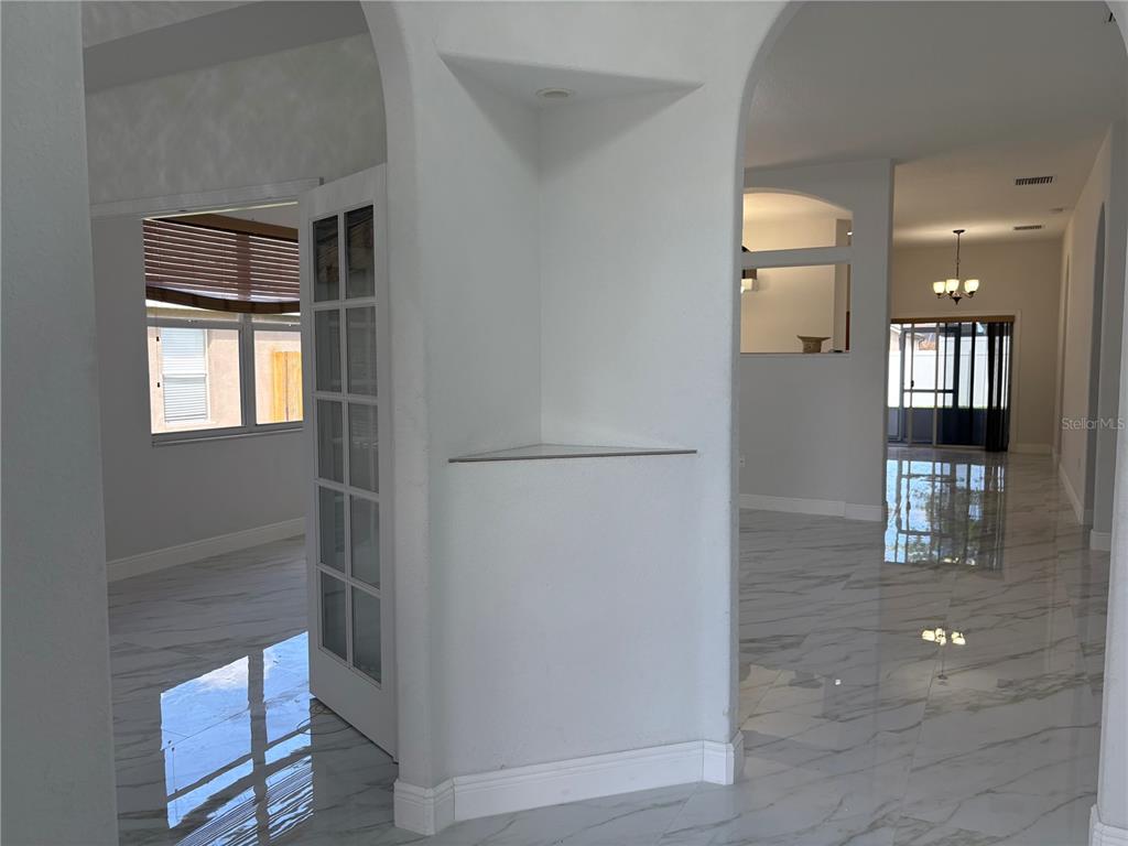 A bright interior space features white arched walls, marble-look tile flooring, and a glass-paneled door — 1150 CREEKVIEW, ST CLOUD, FL