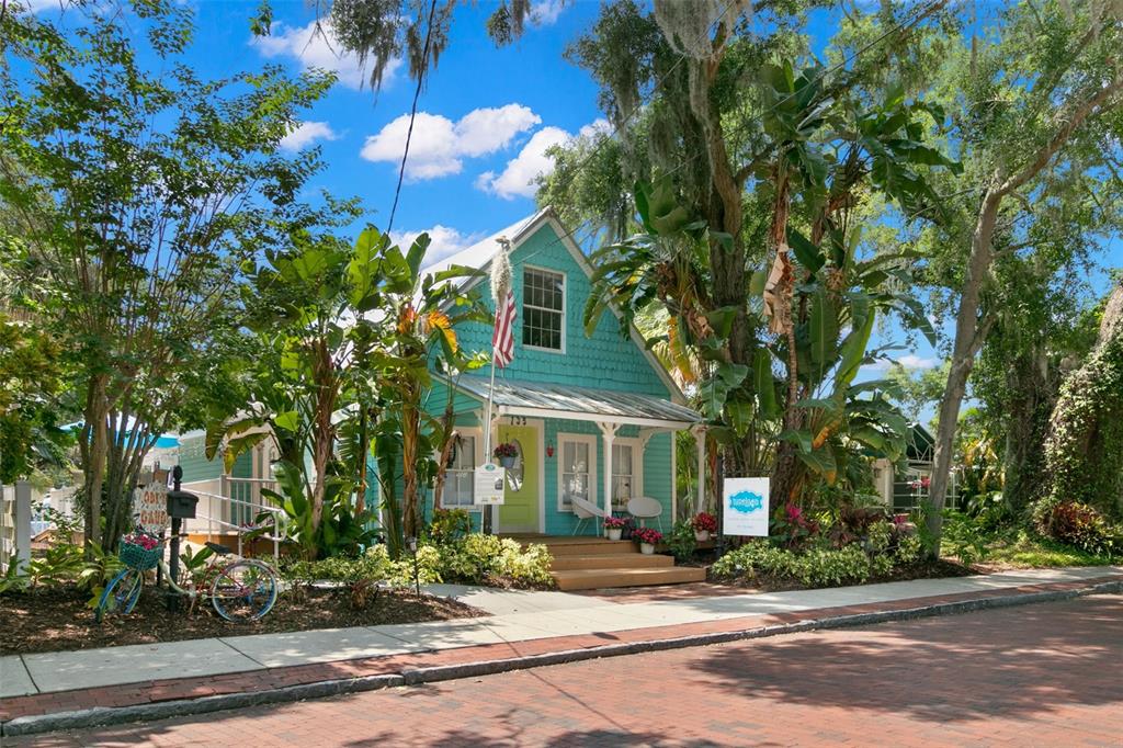 A turquoise cottage with a front porch and American flag sits along a brick street — 135 4TH AVENUE N, SAFETY HARBOR, FL