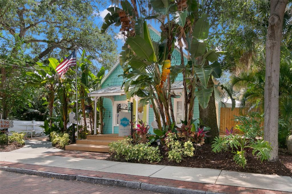 A turquoise cottage with a front porch, American flag, and lush landscaping sits along a sidewalk — 135 4TH AVENUE N, SAFETY HARBOR, FL
